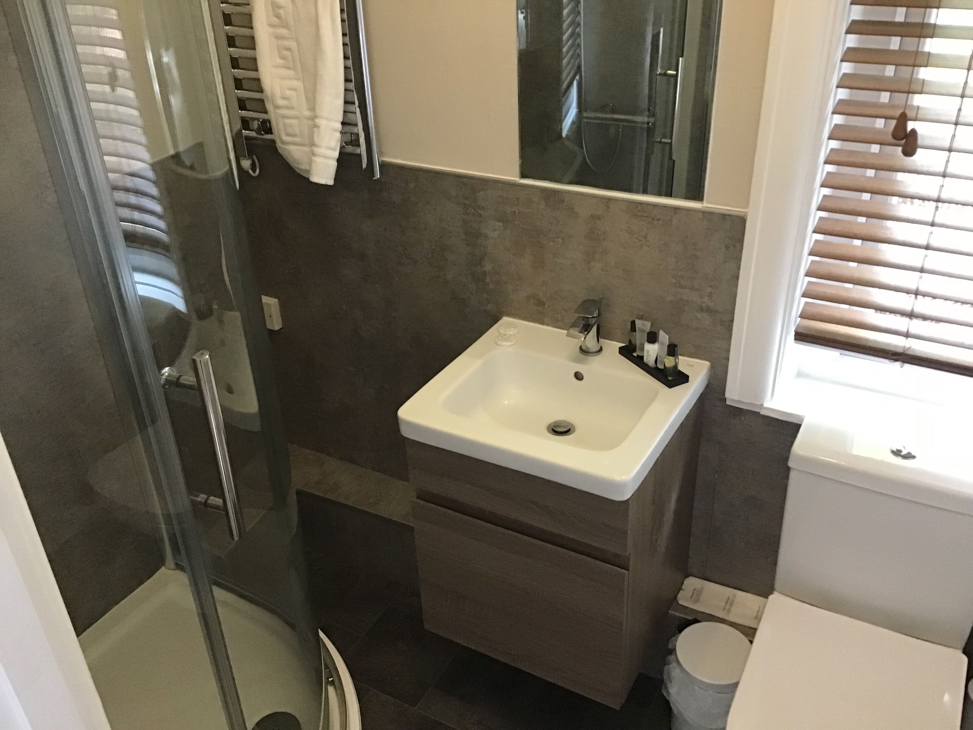 A bathroom with a glass shower enclosure, a white sink with a mirror above it, and a toilet.
