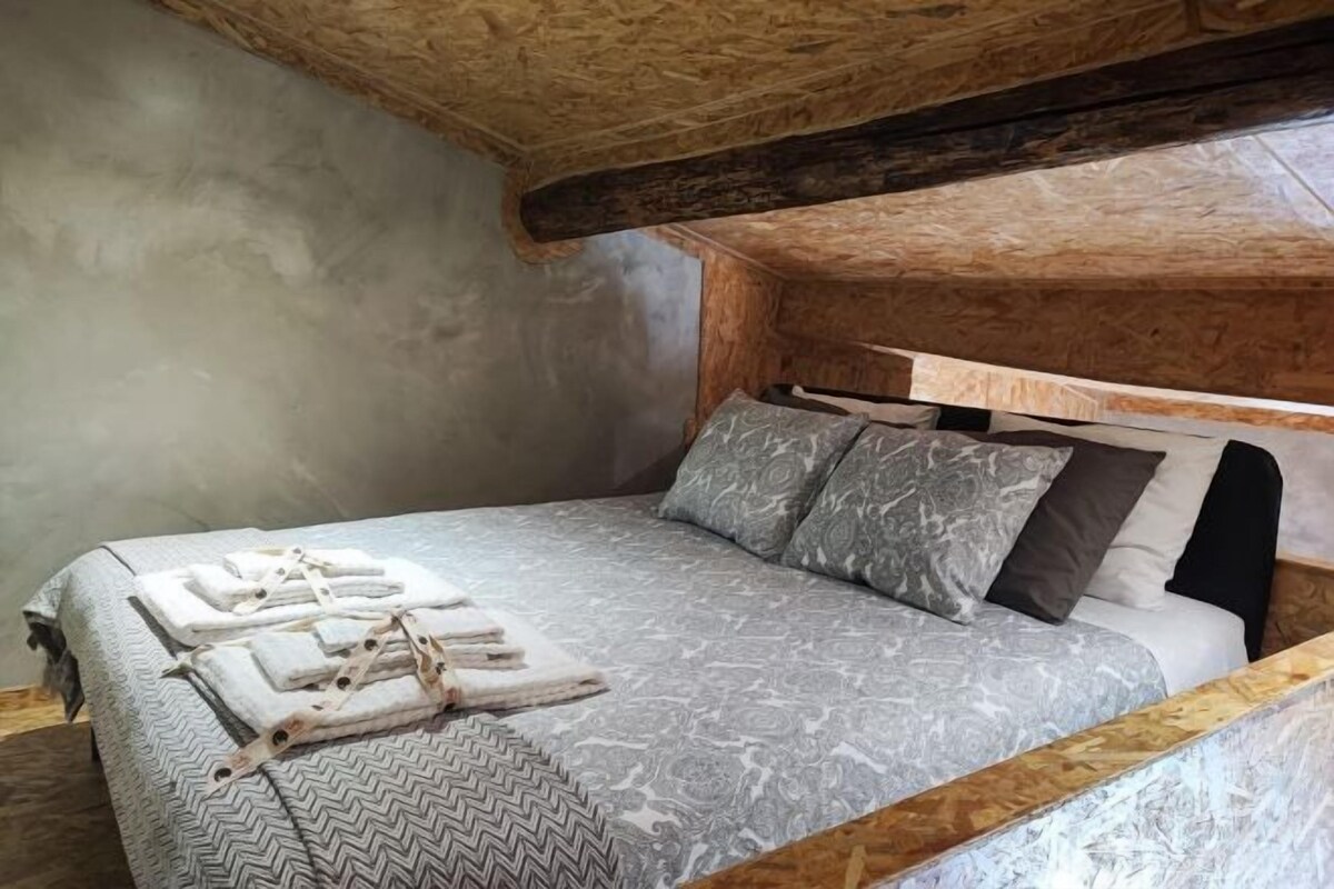 A bedroom with a wooden ceiling, a bed with patterned bedding, and neatly folded towels on the bed.