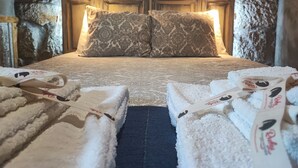 Una cama con almohadones estampados, una pared de piedra y un cabecero de madera.