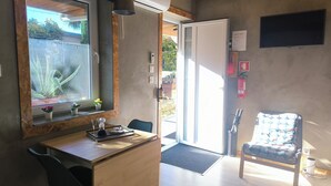 Una habitación moderna con un escritorio de madera, una silla, un ventanal con plantas, una puerta y un televisor en la pared.
