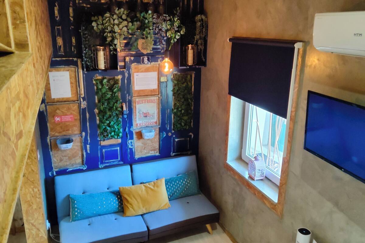 A cozy room with a blue sofa, decorative wall panels, a window with a view, and an air conditioning unit.