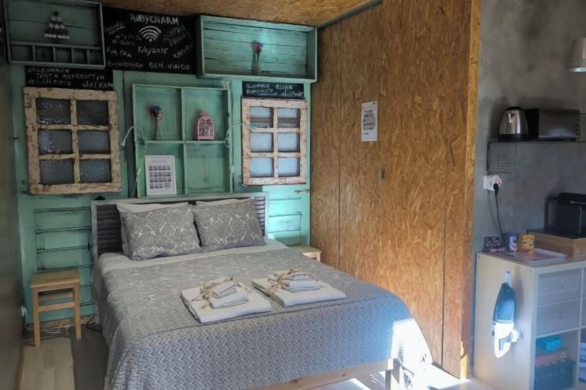 A cozy room with a bed, a small stool, a shelf with a vase, and a wooden cabinet with a kettle.