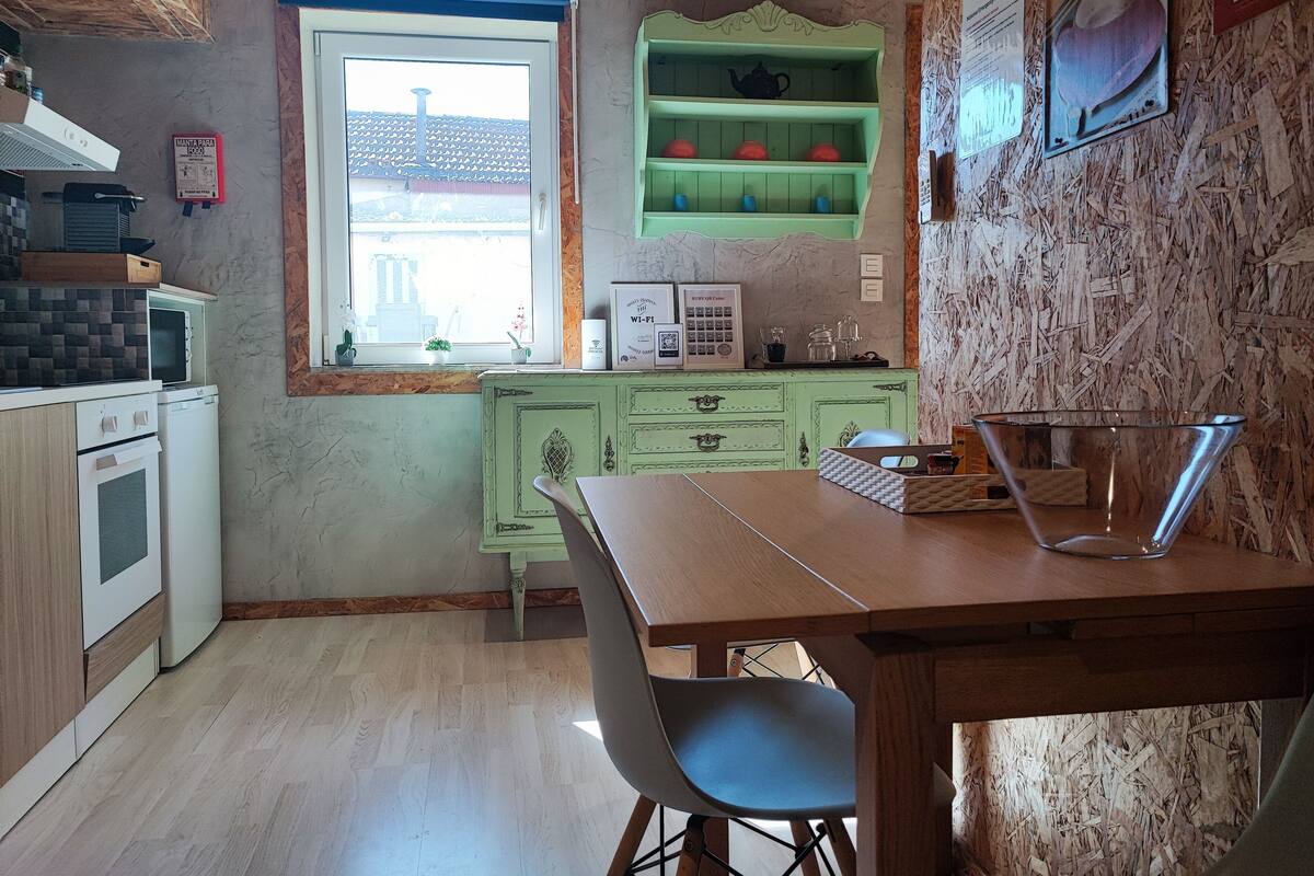 A kitchen with a window, green cabinets, a microwave, and a table with a chair.