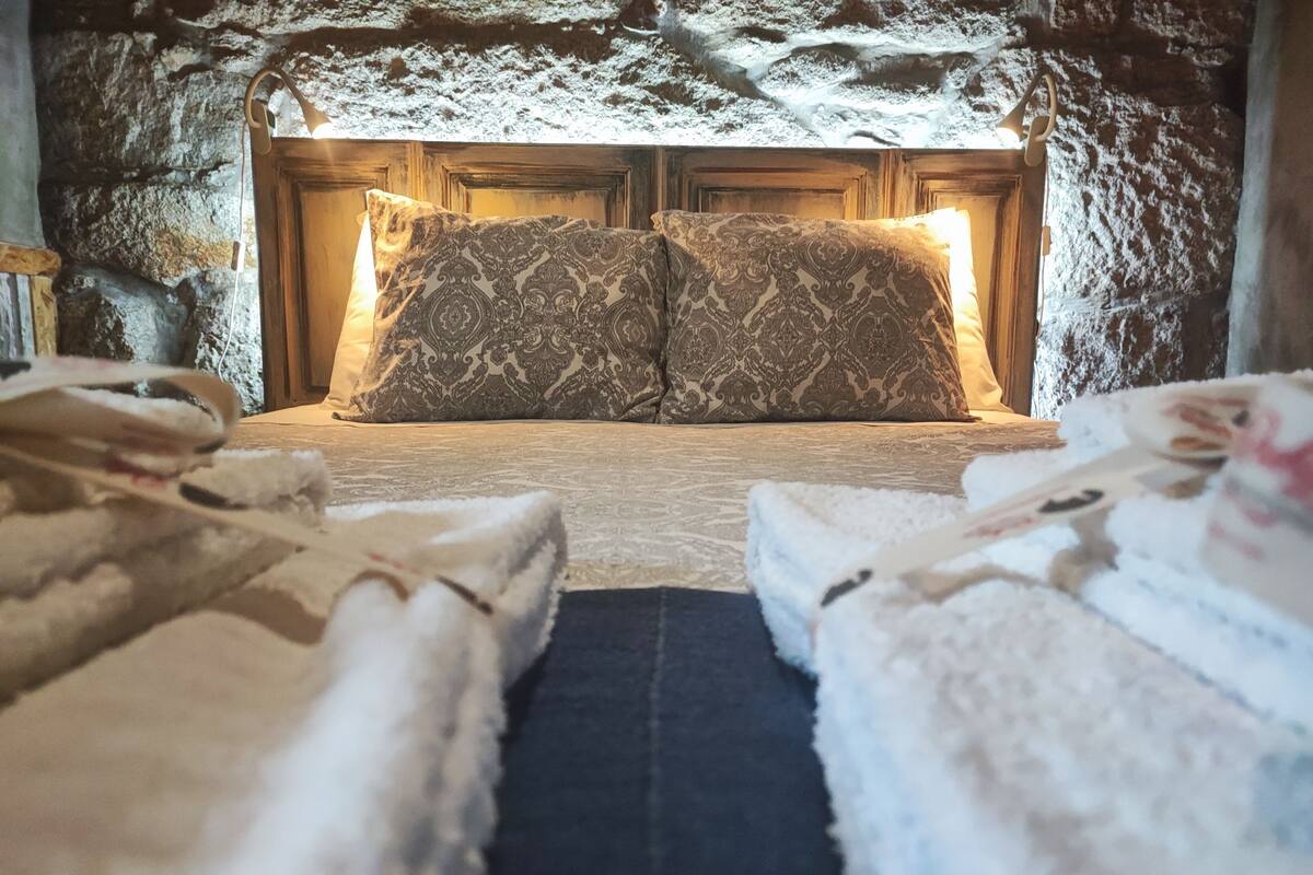 A cozy room with a stone wall, a wooden door, and two beds with patterned pillows.