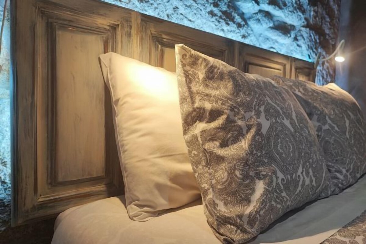 A bed with two pillows, one plain and one patterned, in a room with wooden paneling and a textured wall.