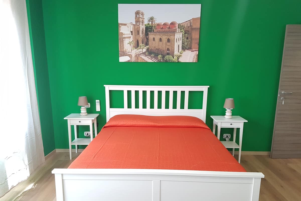 A room with a bed, green walls, a picture of a building, and two bedside tables with lamps.