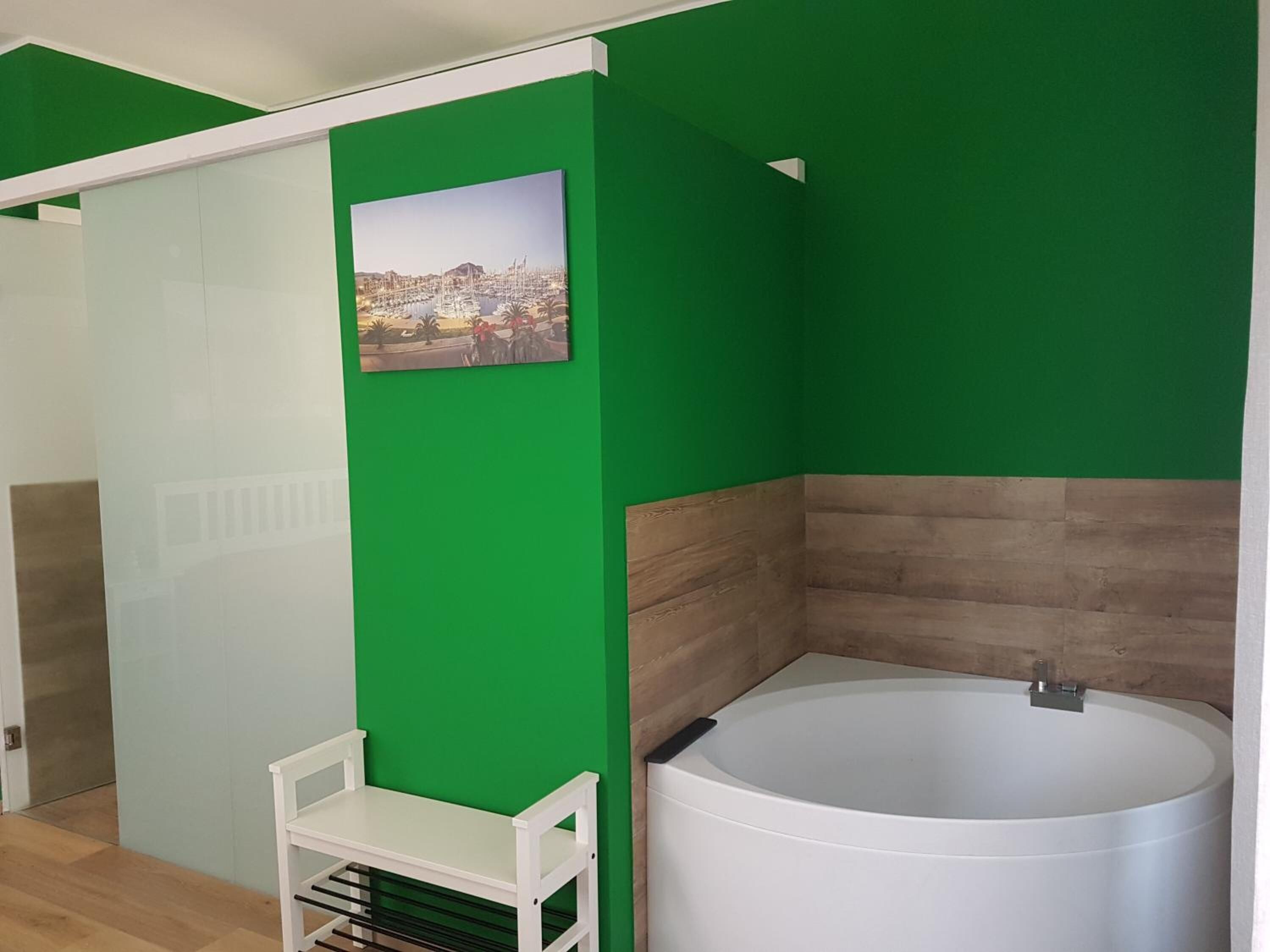 A bathroom with a white bathtub, a green wall, and a picture of a cityscape.