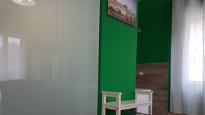 Una habitación con una pared de acento verde, una pequeña silla blanca, suelo de madera y una fotografía de un paisaje urbano.