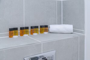 A bathroom with grey tiles, a white towel, and several bottles of Aqua Viva on a shelf. - The Central Lodge (Dartford)