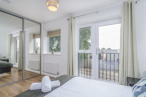 A modern bedroom with a large bed, a mirror, a window with a view of the street, and a radiator. - The Central Lodge (Dartford)
