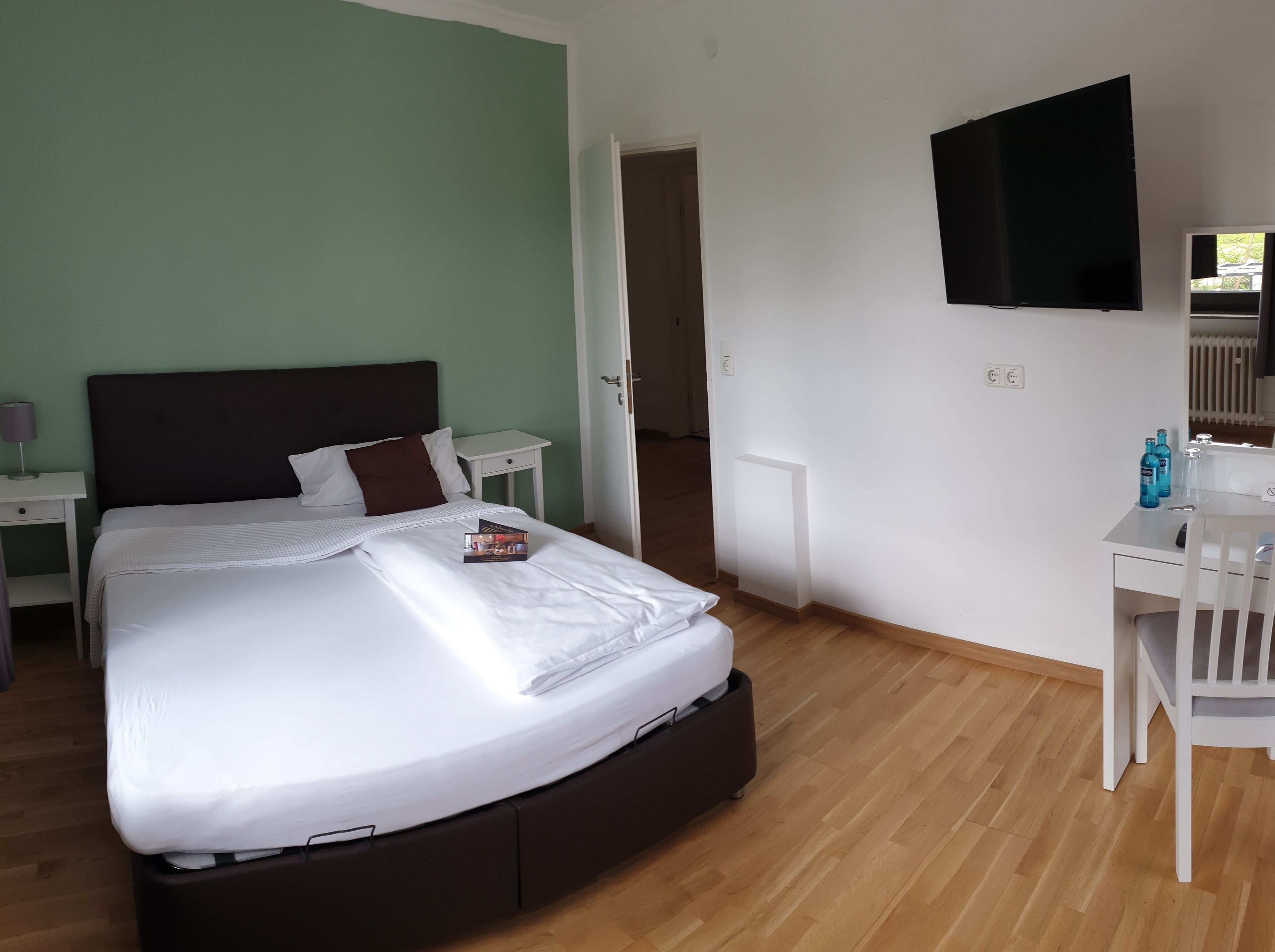 A neatly arranged bedroom with a bed, bedside tables, a desk, and a television.