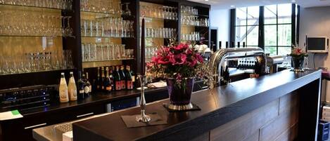 A bar area with shelves of glasses and bottles, a counter with a vase of flowers, and a grill.