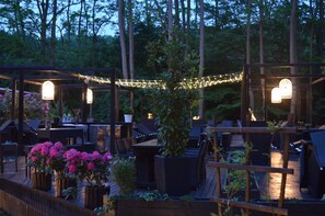 An outdoor patio area with wooden tables and chairs, string lights, and potted plants.