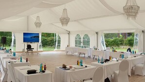 Un espacio para eventos con carpas, mesas dispuestas para una reunión, una pantalla y un altavoz.