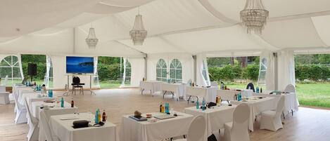 A tented event space with tables set for a gathering, a screen, and a speaker.