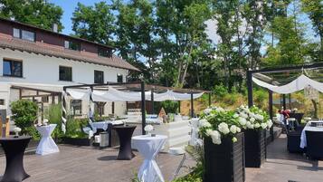 An outdoor patio area with tables and chairs, white canopies, and a large planter with white flowers.
