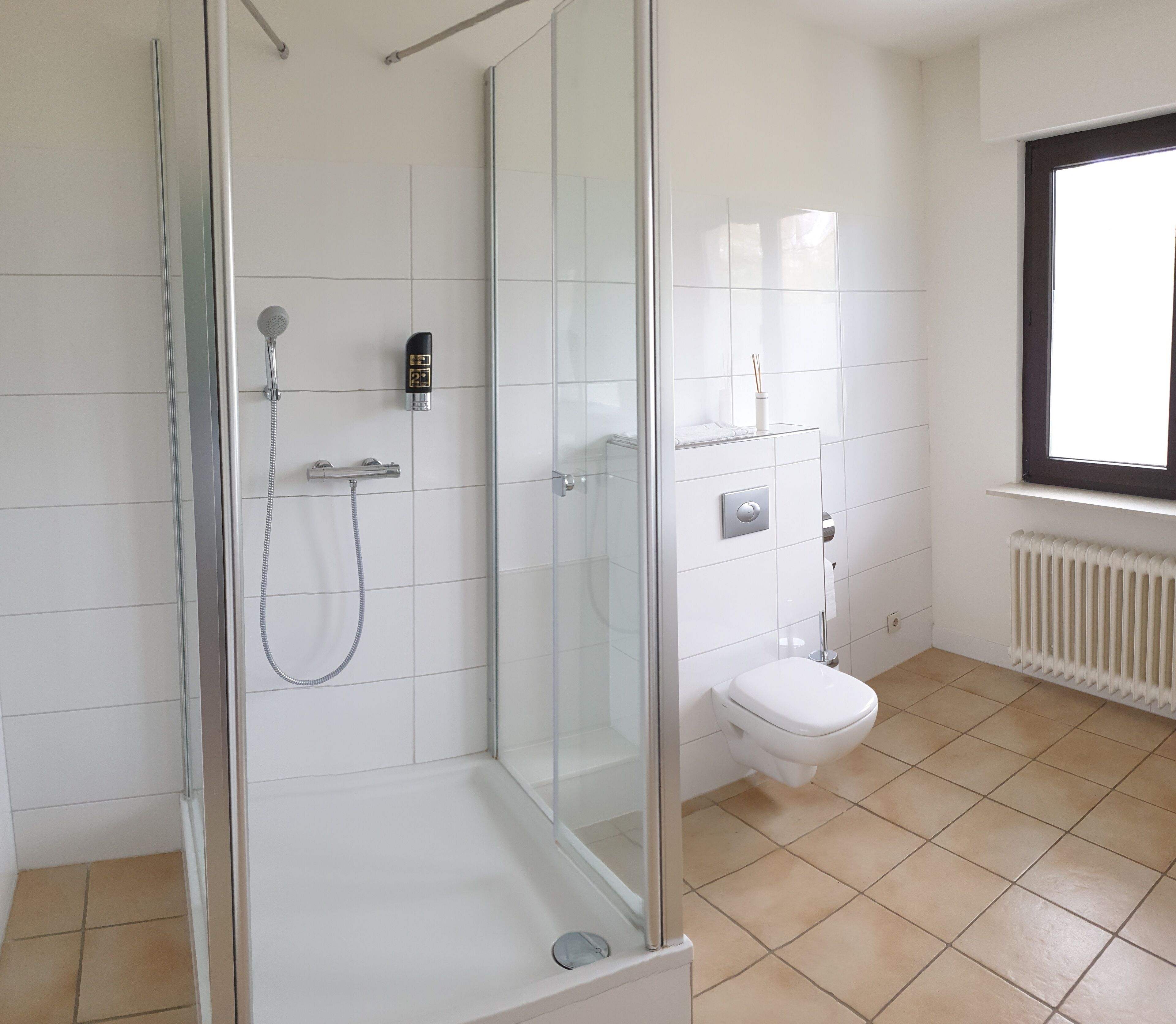 A modern bathroom with a glass-enclosed shower, a toilet, and a window providing natural light.