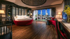 A modern hotel room with a large bed, a red sofa, and a view of the cityscape through large windows. - Shining Central Hotel & Spa (Hanoi)