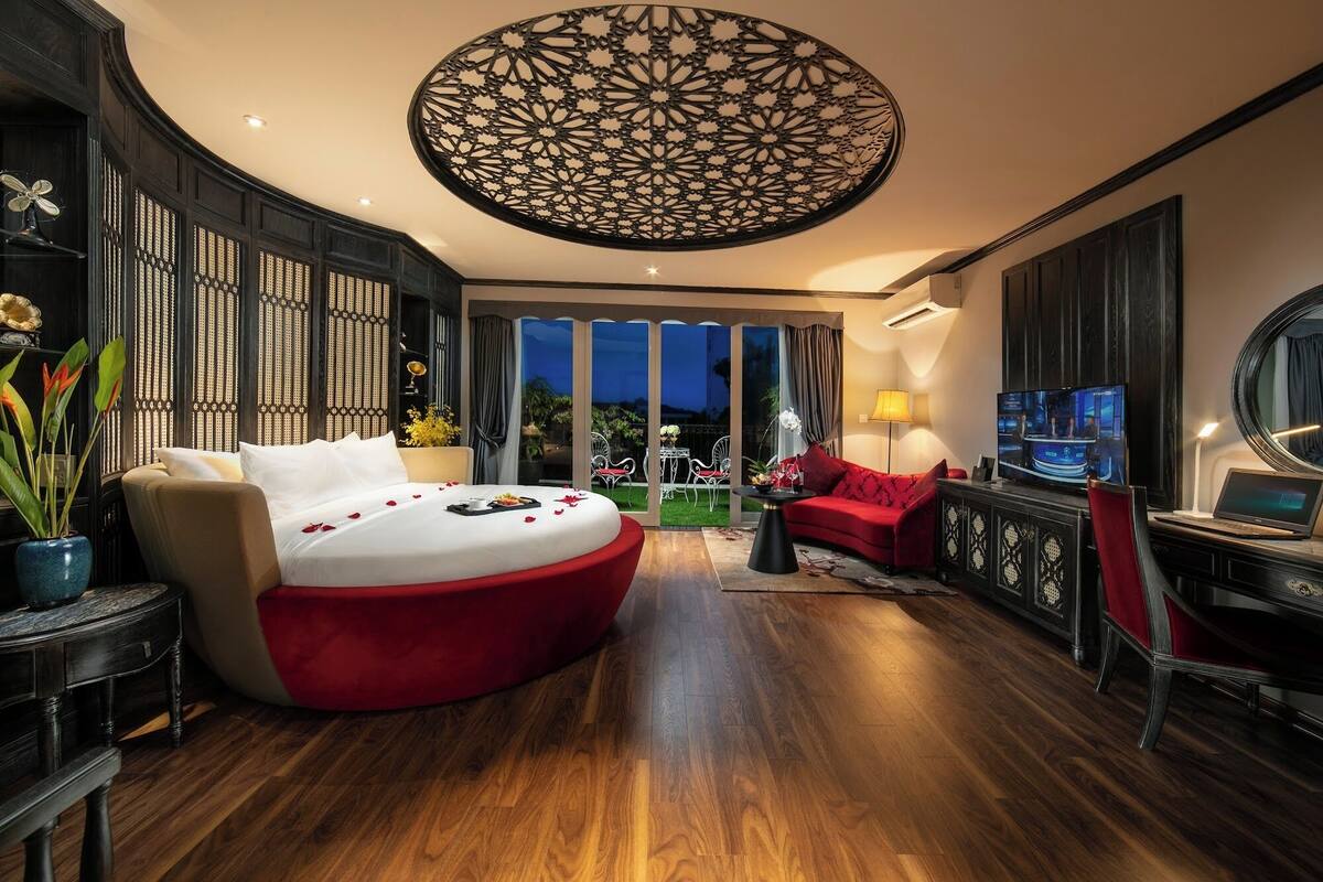 A spacious bedroom with a large bed, a red sofa, a TV, and a decorative ceiling.