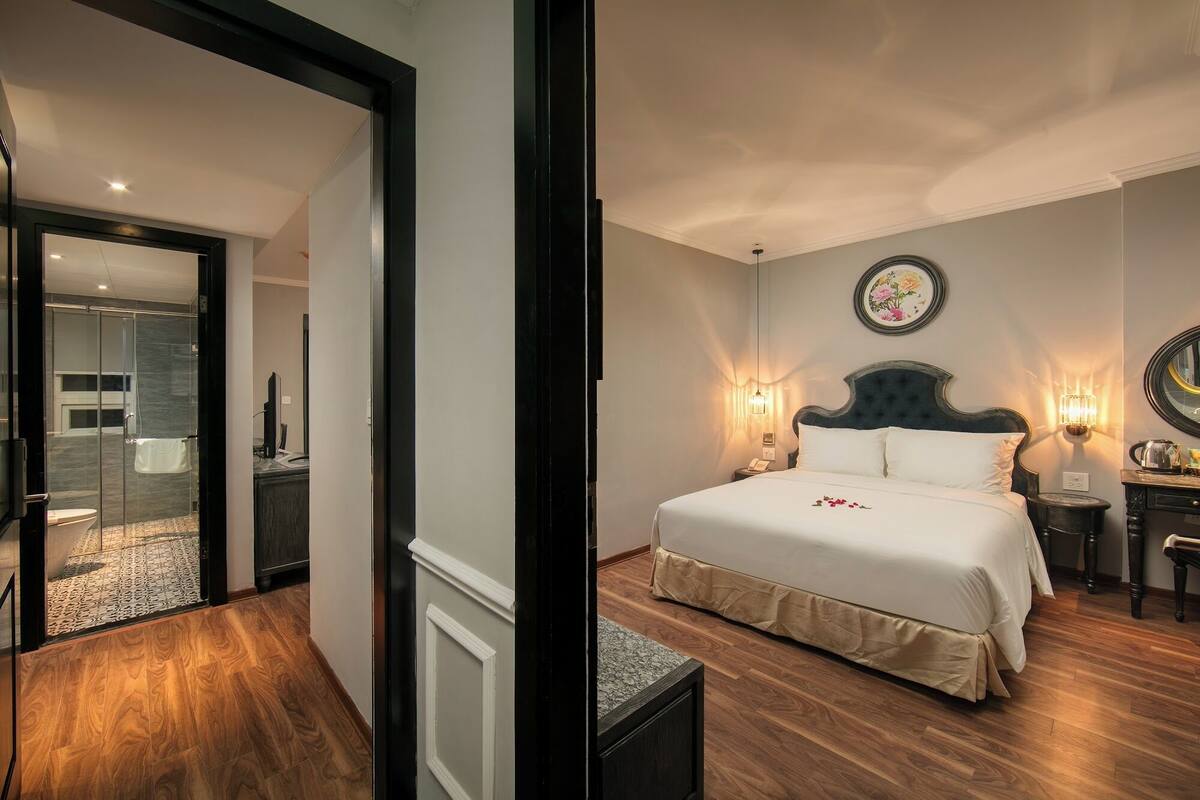 A hotel room with a bed, bedside table, wall-mounted light, and a mirror.