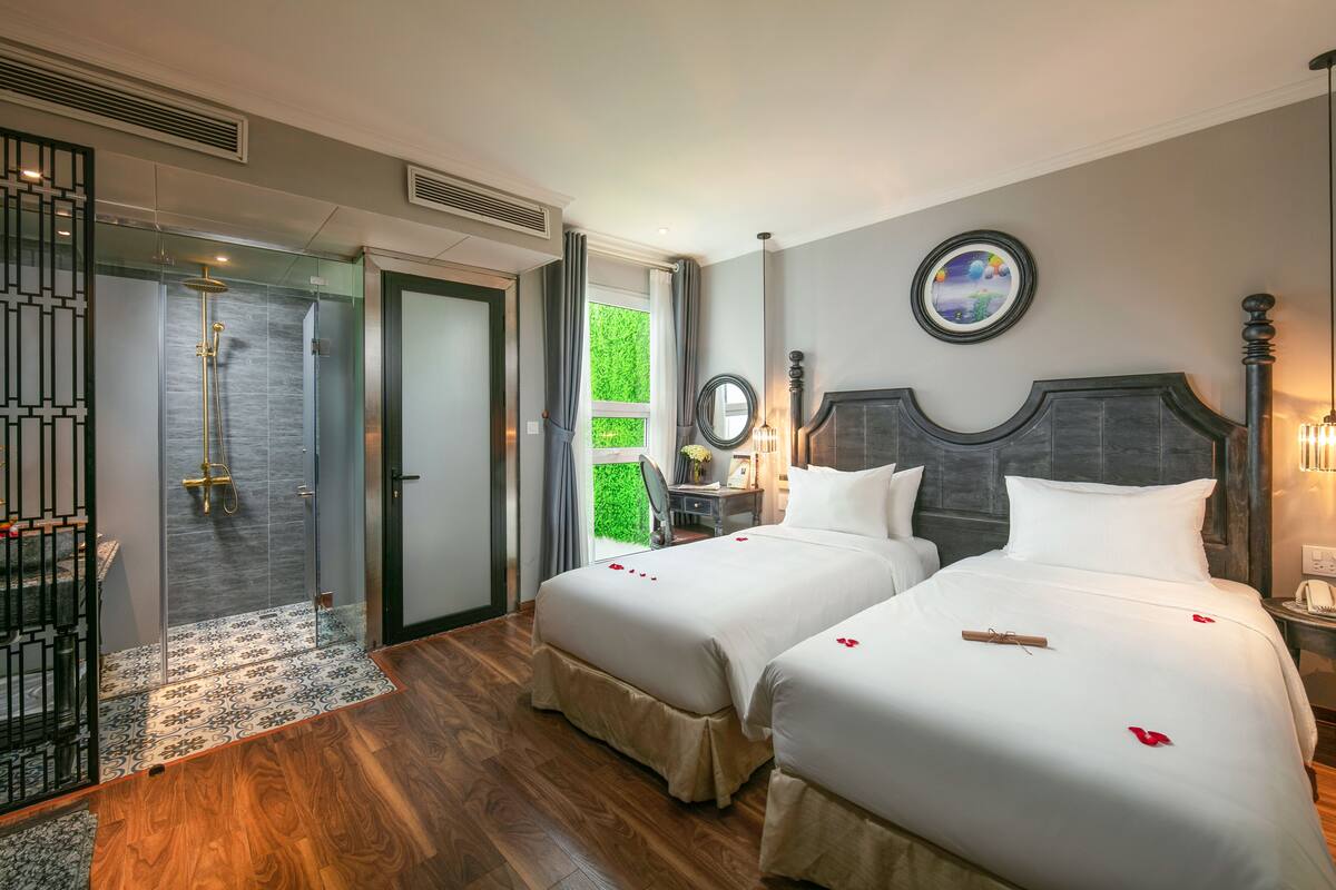 A hotel room with two beds, a shower, and a view of greenery.