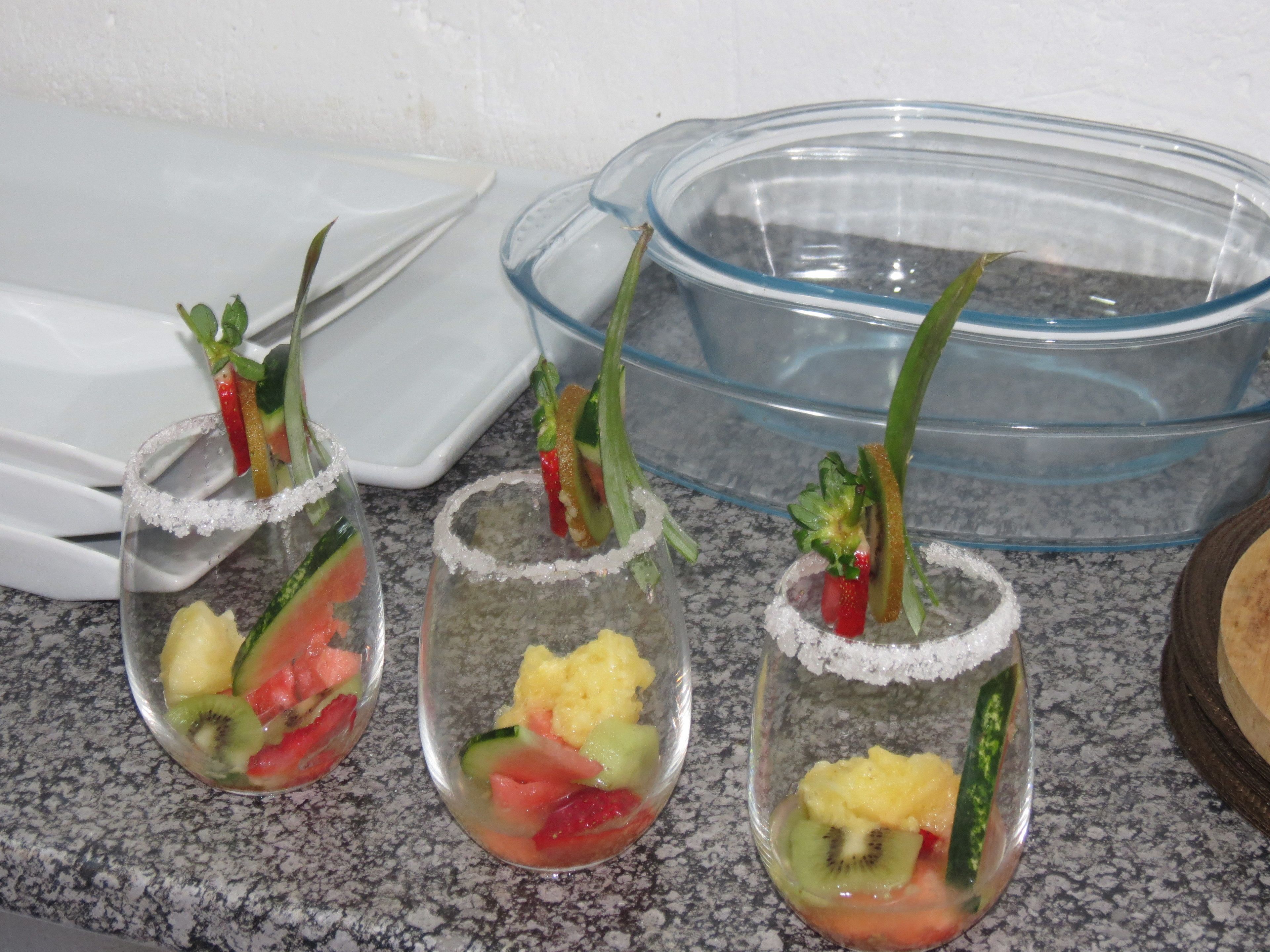 Three clear glasses with fruit and a sugar rim, placed on a granite countertop.