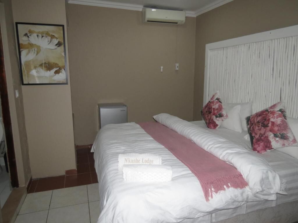 A hotel room with a bed, a bedside table, a wall-mounted air conditioner, and a framed artwork.