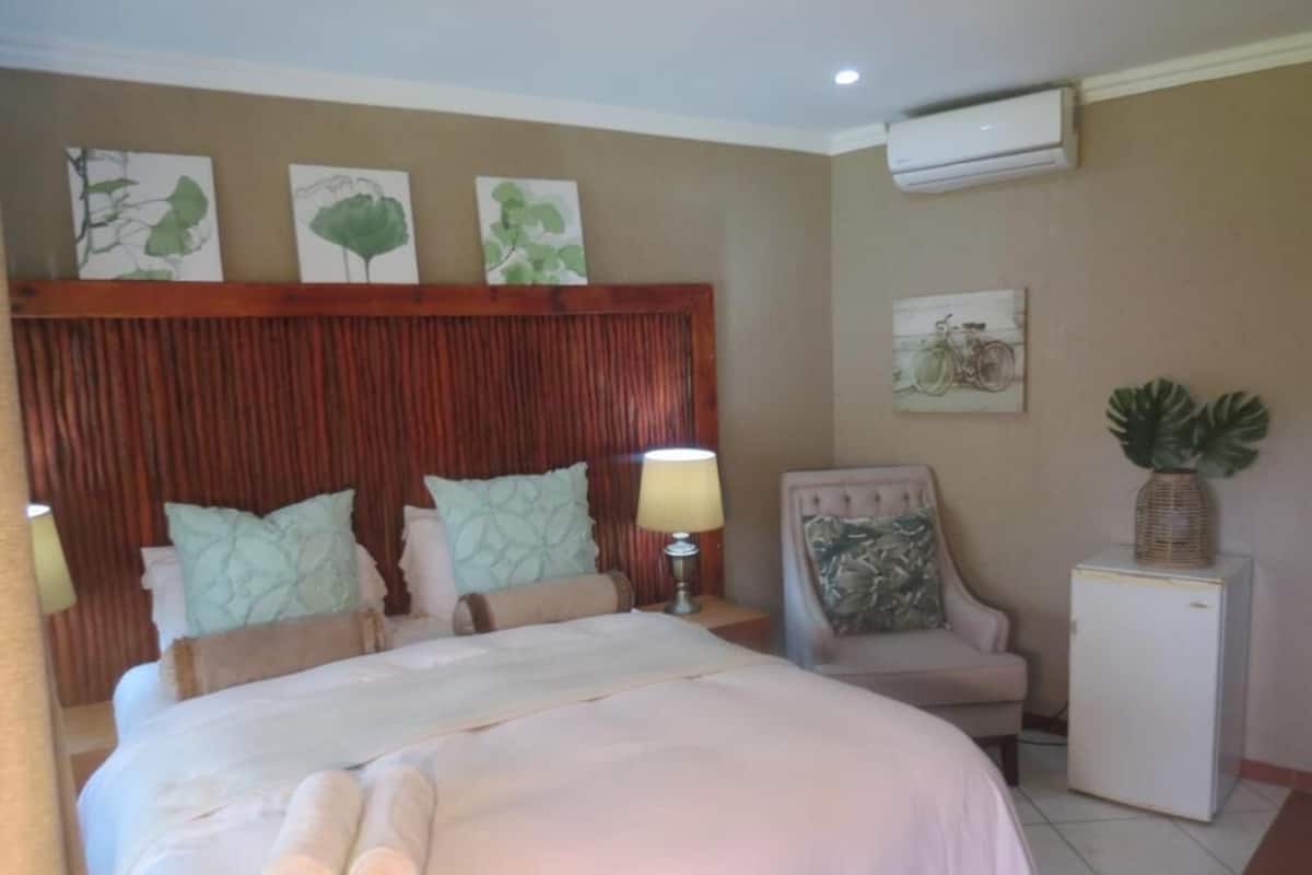 A hotel room with a bed, a chair, a small table, and an air conditioning unit.