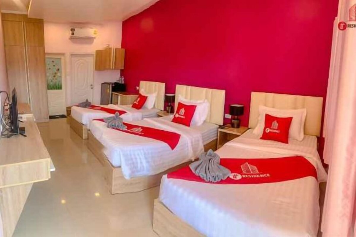Une chambre d’hôtel avec trois lits, chacun agrémenté de draps blancs et de touches de couleur rouge, un bureau en bois et un mur d’un rouge vif.