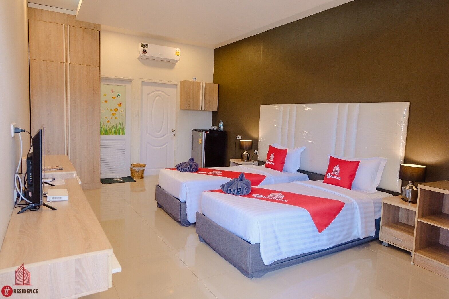 Quarto de hotel com duas camas, uma escrivaninha, televisão, frigorífico e ar condicionado fixado na parede.