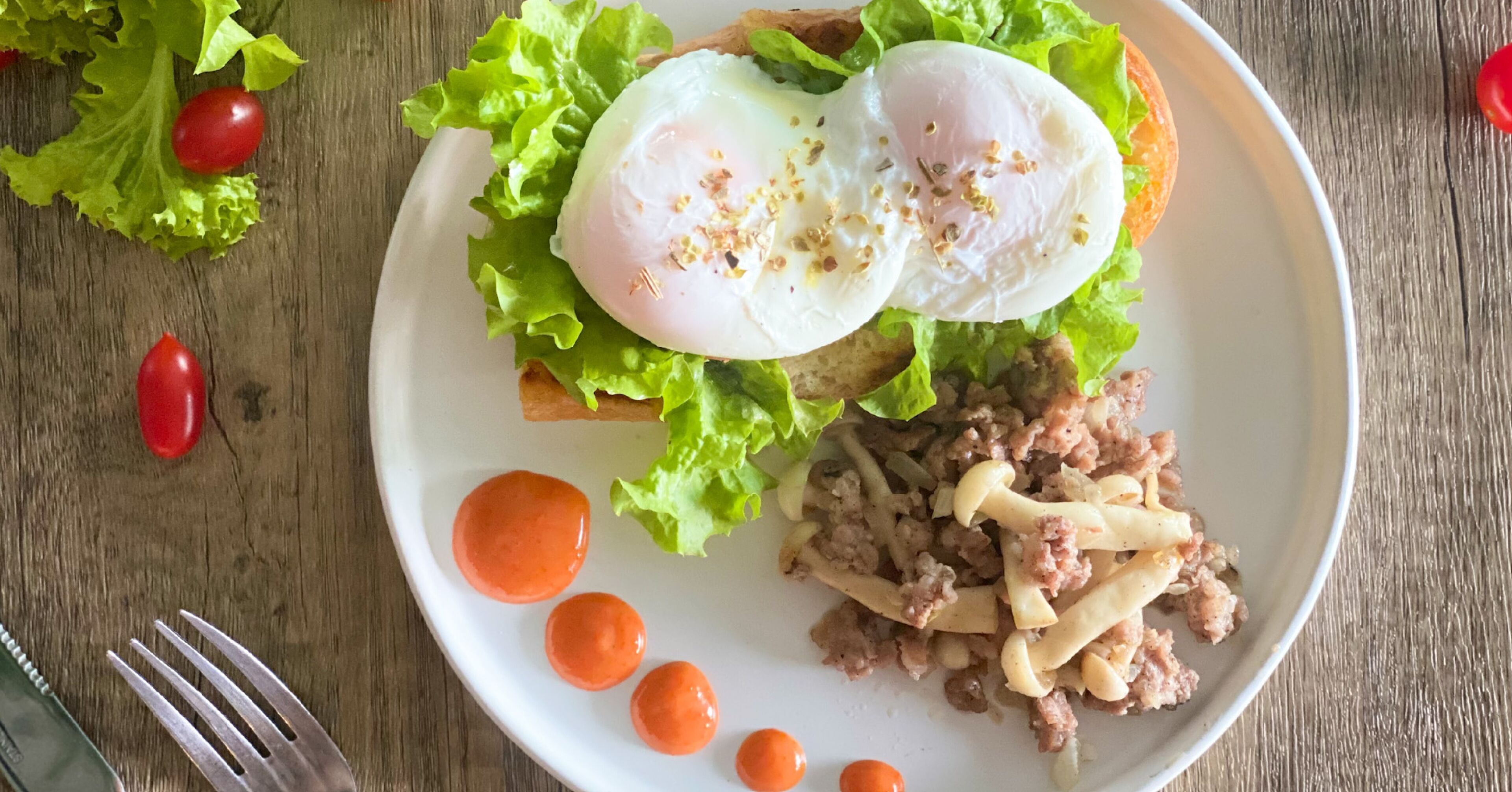 Un plato con sándwich, huevos pochados, lechuga y un guiso de carne, acompañado de un tenedor y salsa.