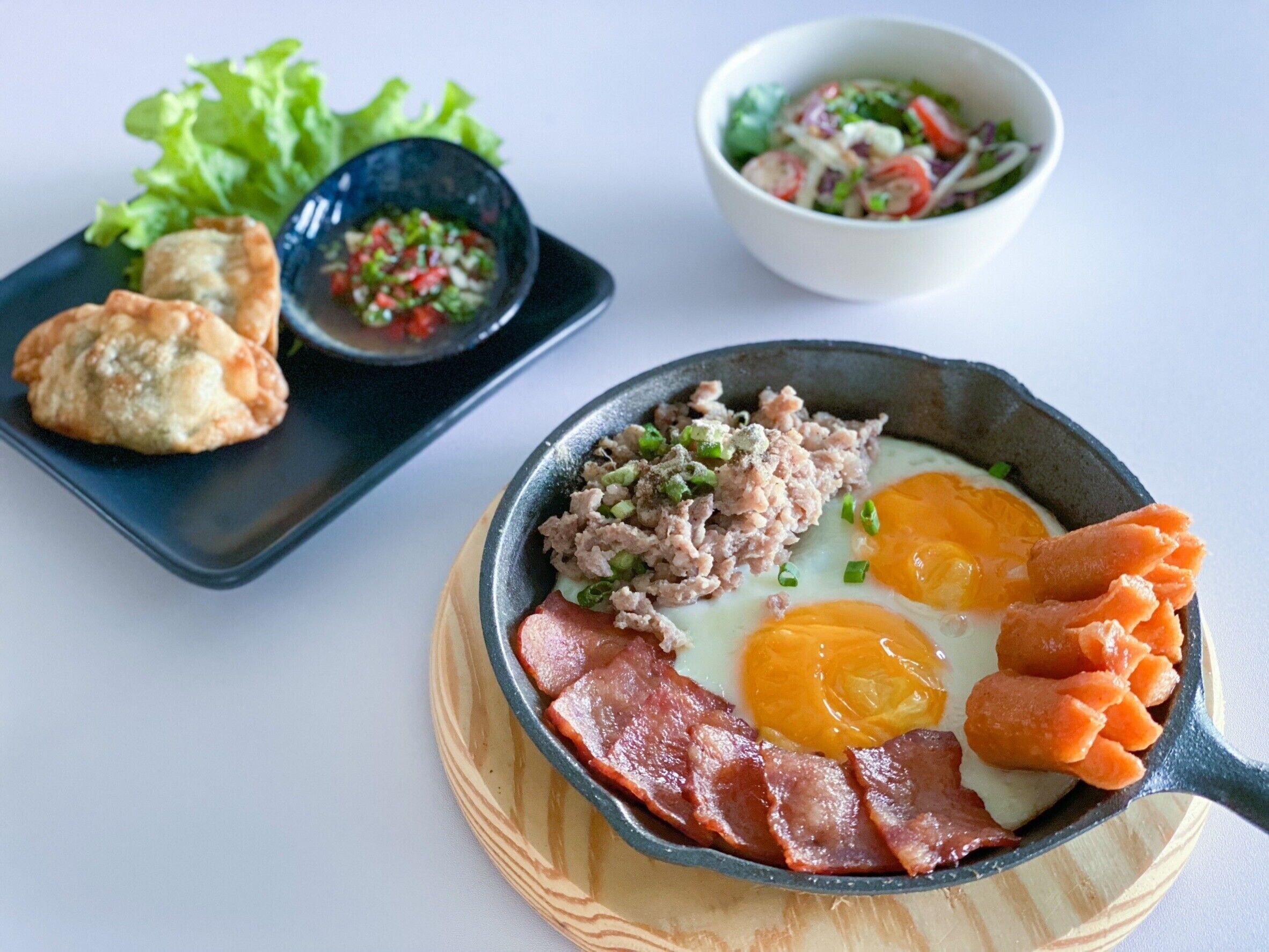 A breakfast plate with eggs, bacon, and sausage, accompanied by a side of salad and a small bowl of salsa.