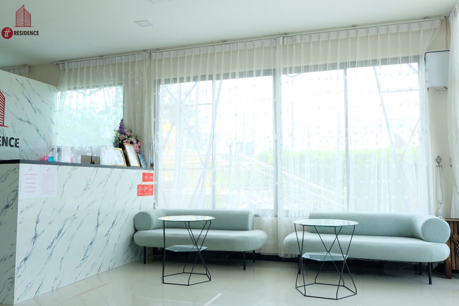 A hotel reception area with a marble reception desk, two sofas, and two small tables.