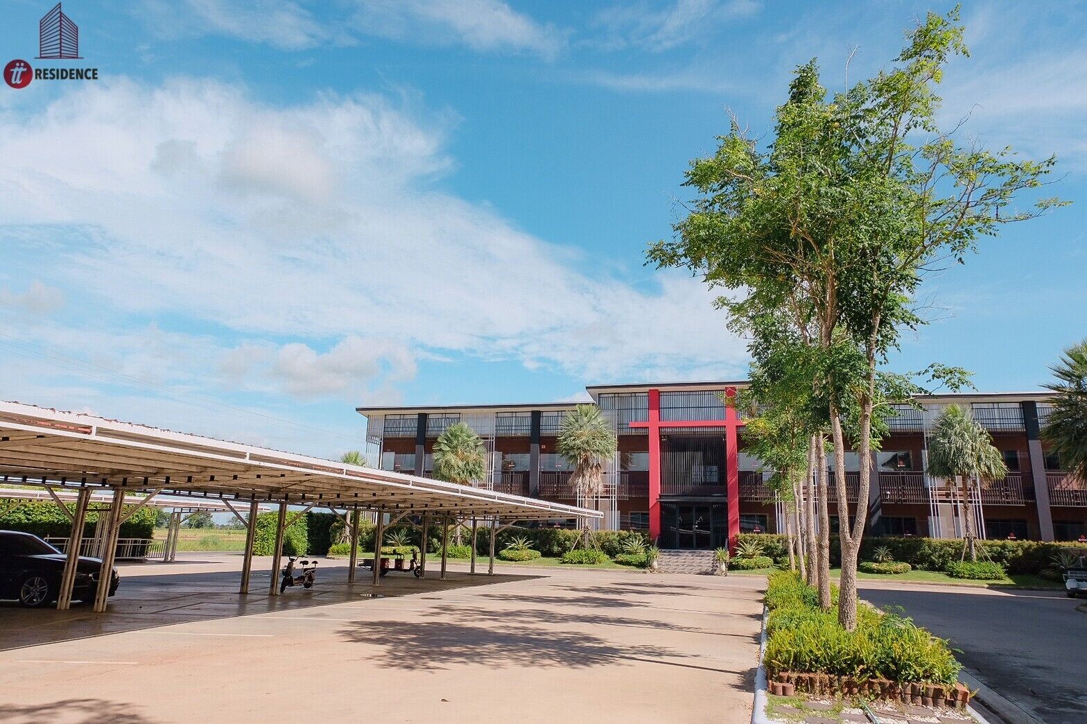 A modern building with a covered parking area, a red entrance, and surrounding greenery.