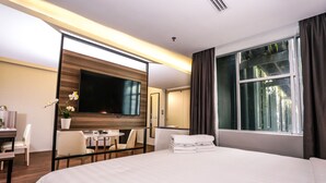 Habitación de hotel con una cama grande, un escritorio con silla, un televisor montado en la pared y una ventana con cortinas.