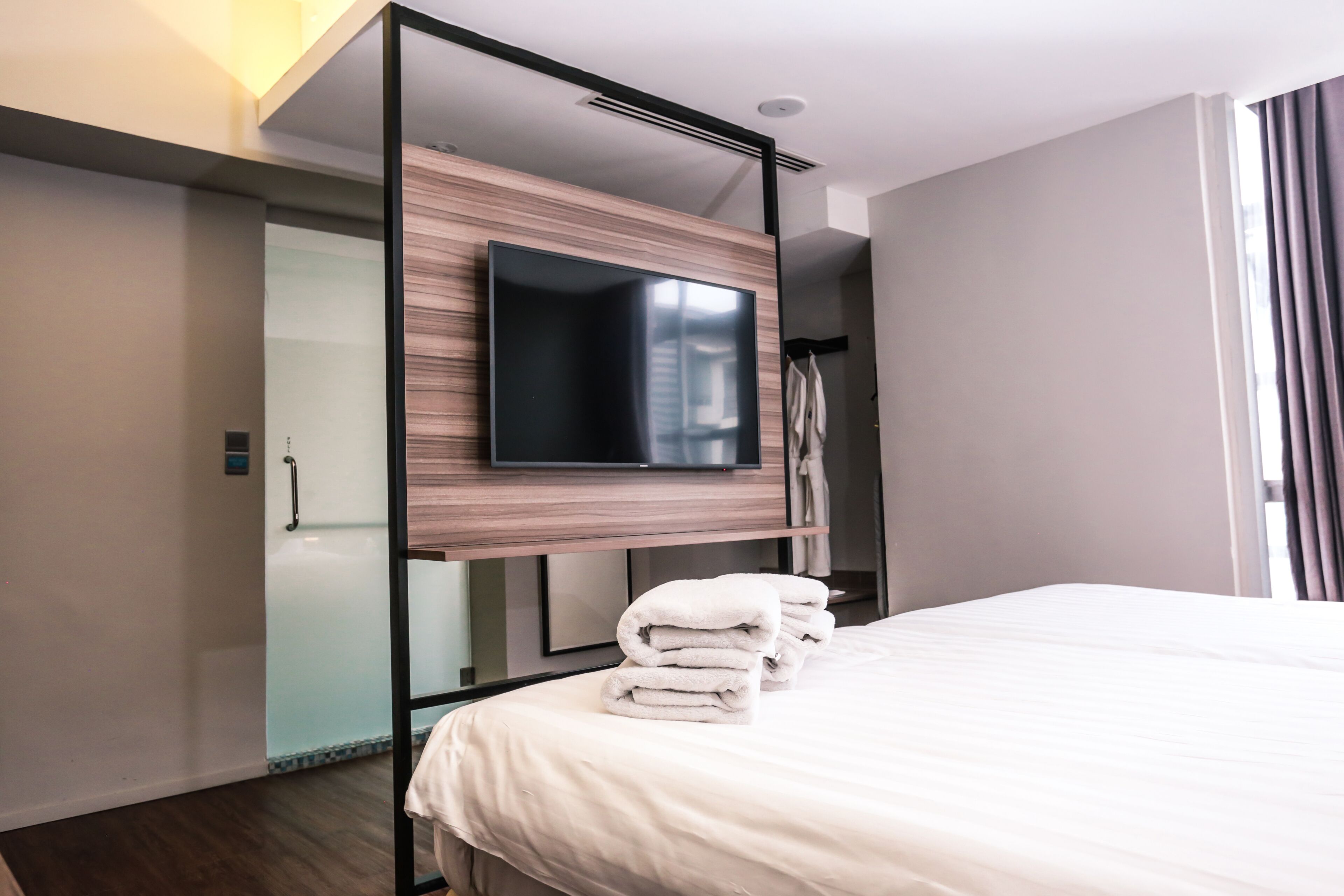 Quarto de hotel moderno com uma cama grande, uma TV de tela plana fixada em um painel de madeira e um box de vidro.