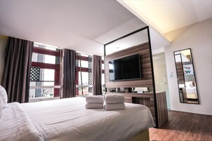 Habitación de hotel con una cama grande, un televisor de pantalla plana montado en la pared, un escritorio con una silla y una ventana con cortinas.