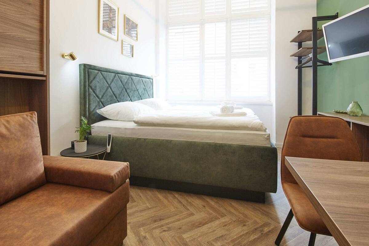 A modern bedroom with a bed, a wooden desk, a brown sofa, and a TV on a stand.