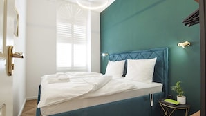 Een slaapkamer met een bed, een nachtkastje, een plant in pot en een raam met luiken.