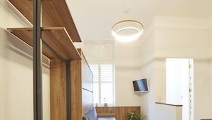 Een modern interieur met een houten trap, een zithoek en een aan de muur bevestigde televisie.