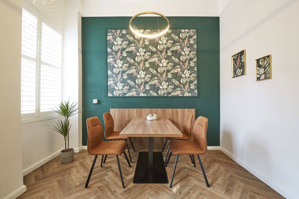 A dining area with a wooden table and four chairs, a potted plant, and a large floral artwork on the wall.