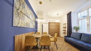 Een moderne eetruimte met een houten tafel en stoelen, een blauwe wand met een groot bloemenkunstwerk, en een blauwe bank met een plant.