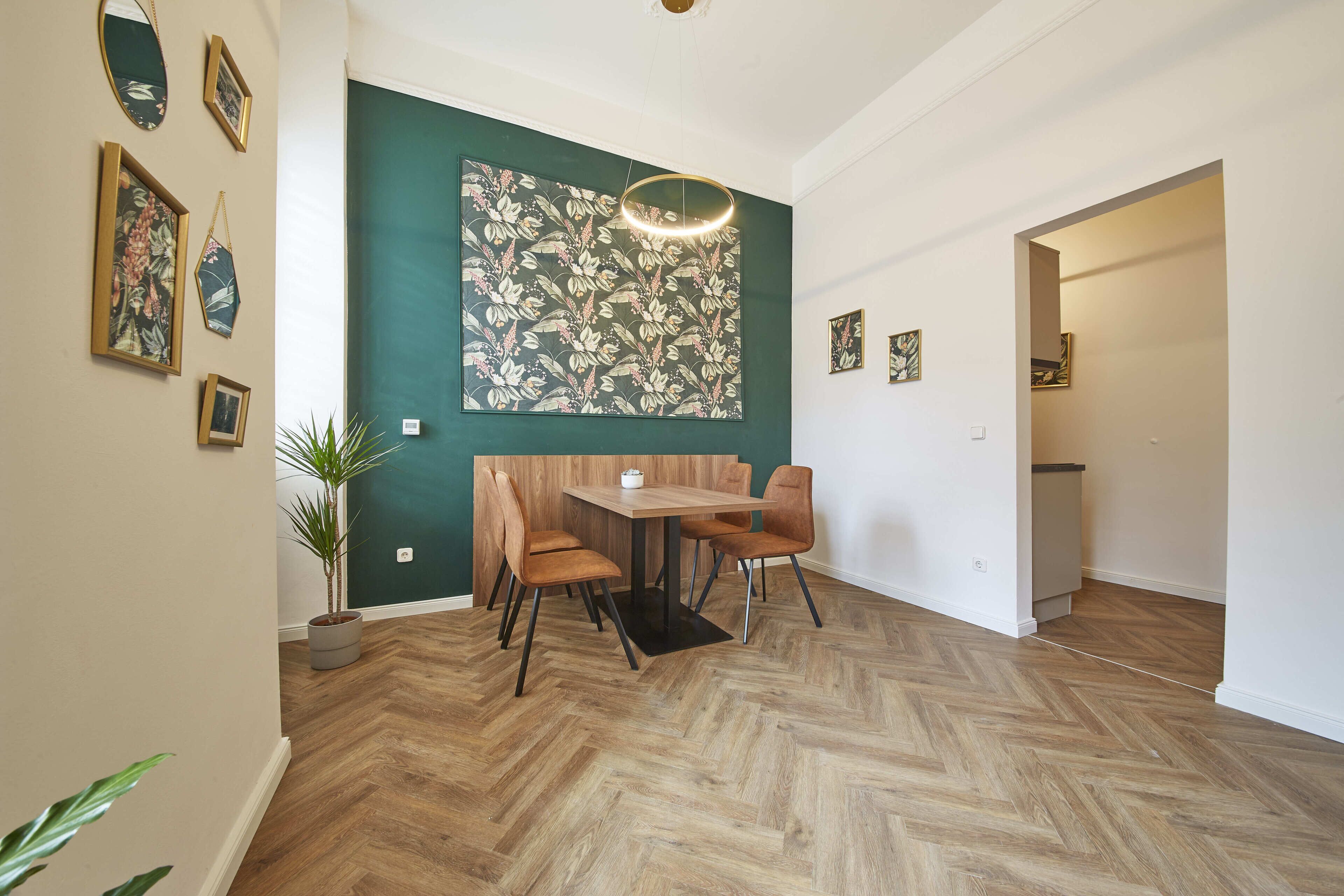 A dining area with a herringbone wooden floor, a table with chairs, and a large floral artwork on the wall.