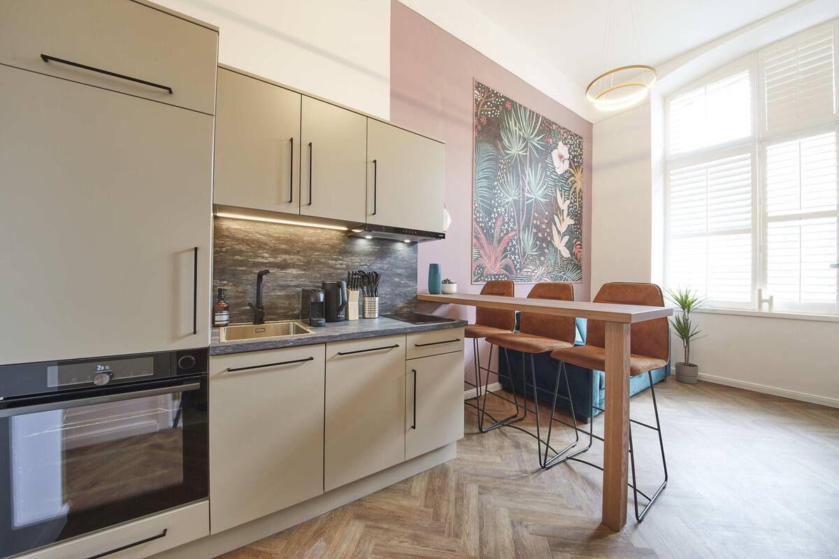 A modern kitchen with built-in appliances, a dining area with a wooden table and chairs, and a large window providing natural light.