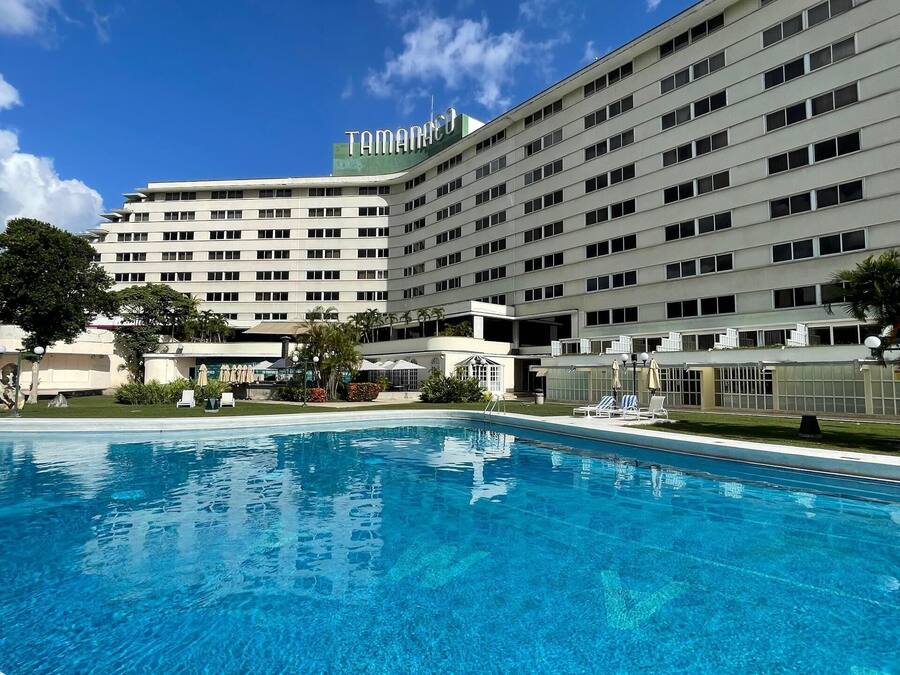 A hotel with a large swimming pool, multiple floors, and a clear blue sky.