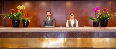 Un mostrador de recepción con dos personas sentadas, rodeado de plantas en macetas.