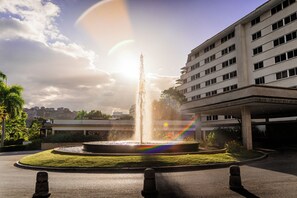 A fountain with water jets, surrounded by a circular grassy area, with a multi-story building in the background. - Hotel Tamanaco Caracas (Caracas)