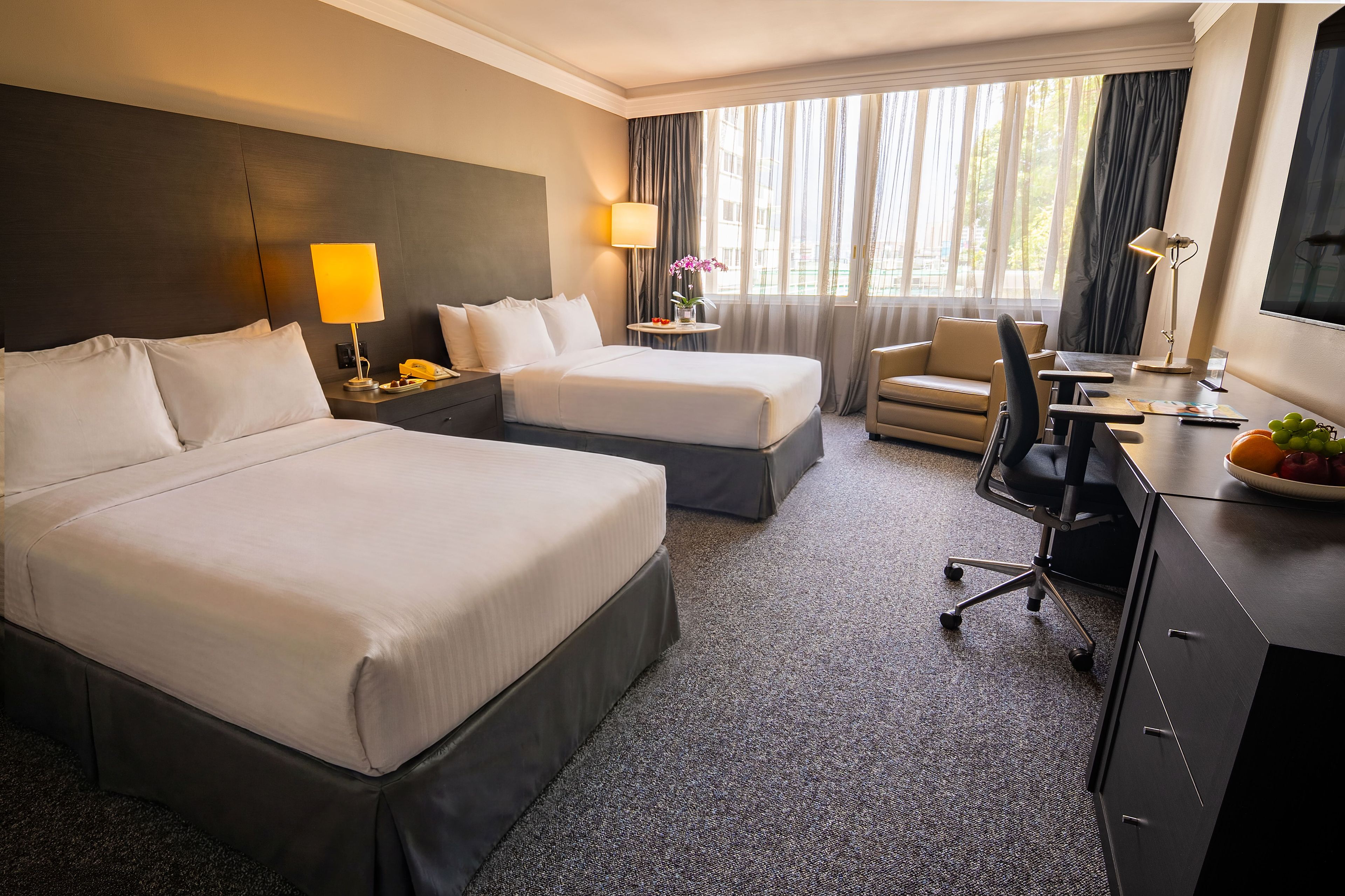 Habitación de hotel con dos camas, un escritorio, una silla, una lámpara y una ventana con cortinas.