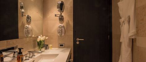 A modern bathroom with a large mirror, two sinks, a towel rack, and a dark door.