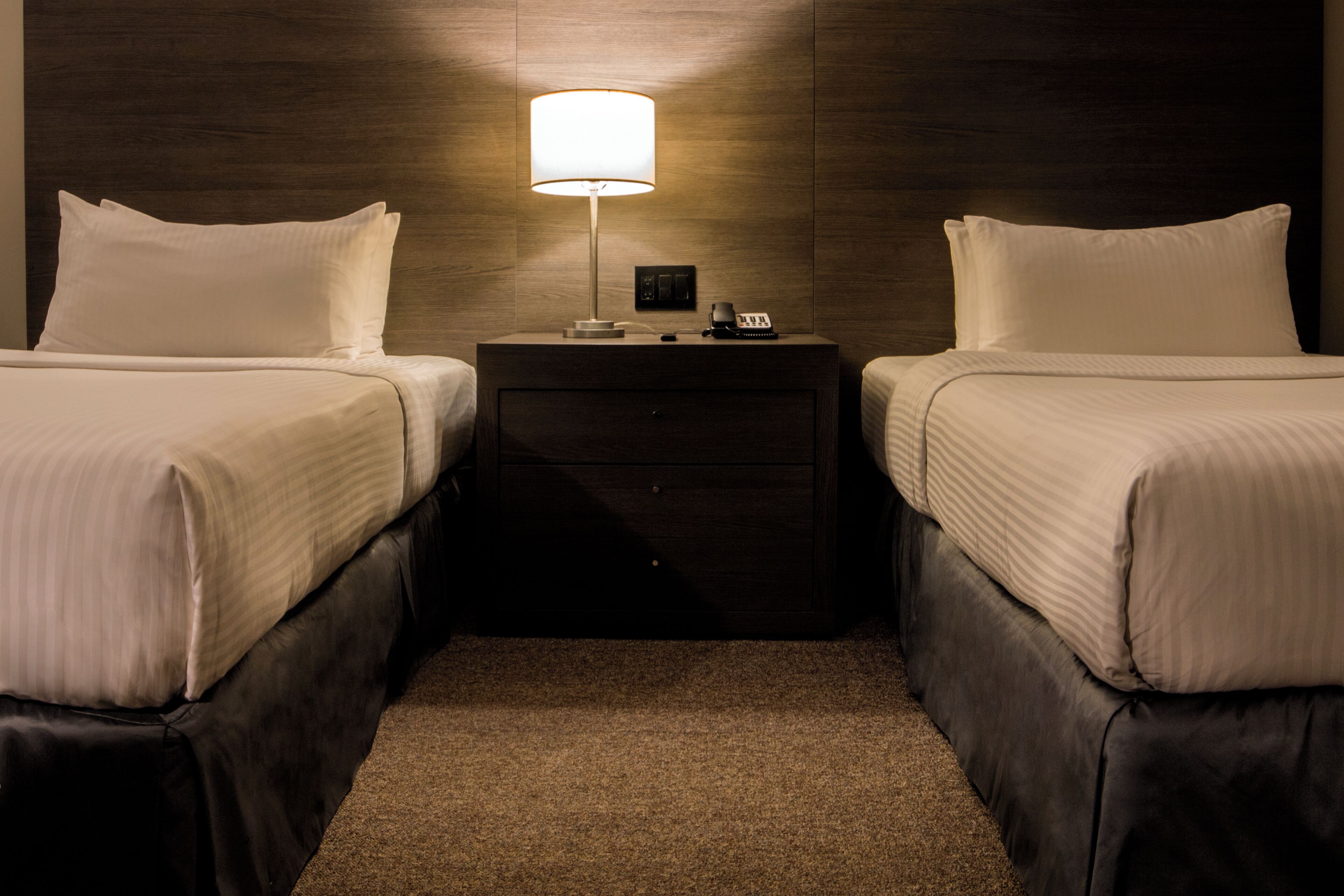 Habitación de hotel con dos camas, una mesita de noche con lámpara, teléfono y un cajón pequeño.